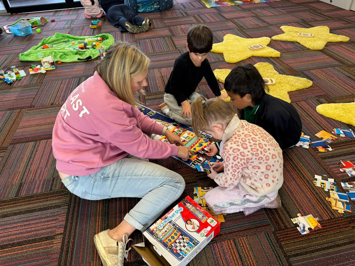 An Eluma early childhood teacher and three children working together on a floor puzzle during a Ready, Set, Grow session